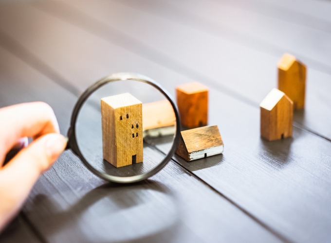 The image shows someone looking at a miniature house through a magnifying glass
